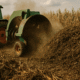 Agriculture Waste Recycling - A compost turner machine churning a large heap of decaying corn and crop waste in an open field near a corn farm, highlighting agricultural waste recycling in action.