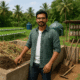 An farmer standing beside a composting unit filled with agricultural waste, surrounded by a lush green farm featuring a biogas plant, hydroponic system, and mushroom cultivation area.